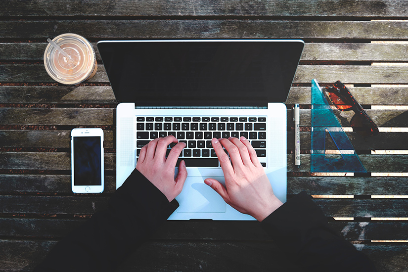 Schreibend bleibt die Welt stehen Foto von oben auf Hände am Laptop von Stanley Dai, Unsplash